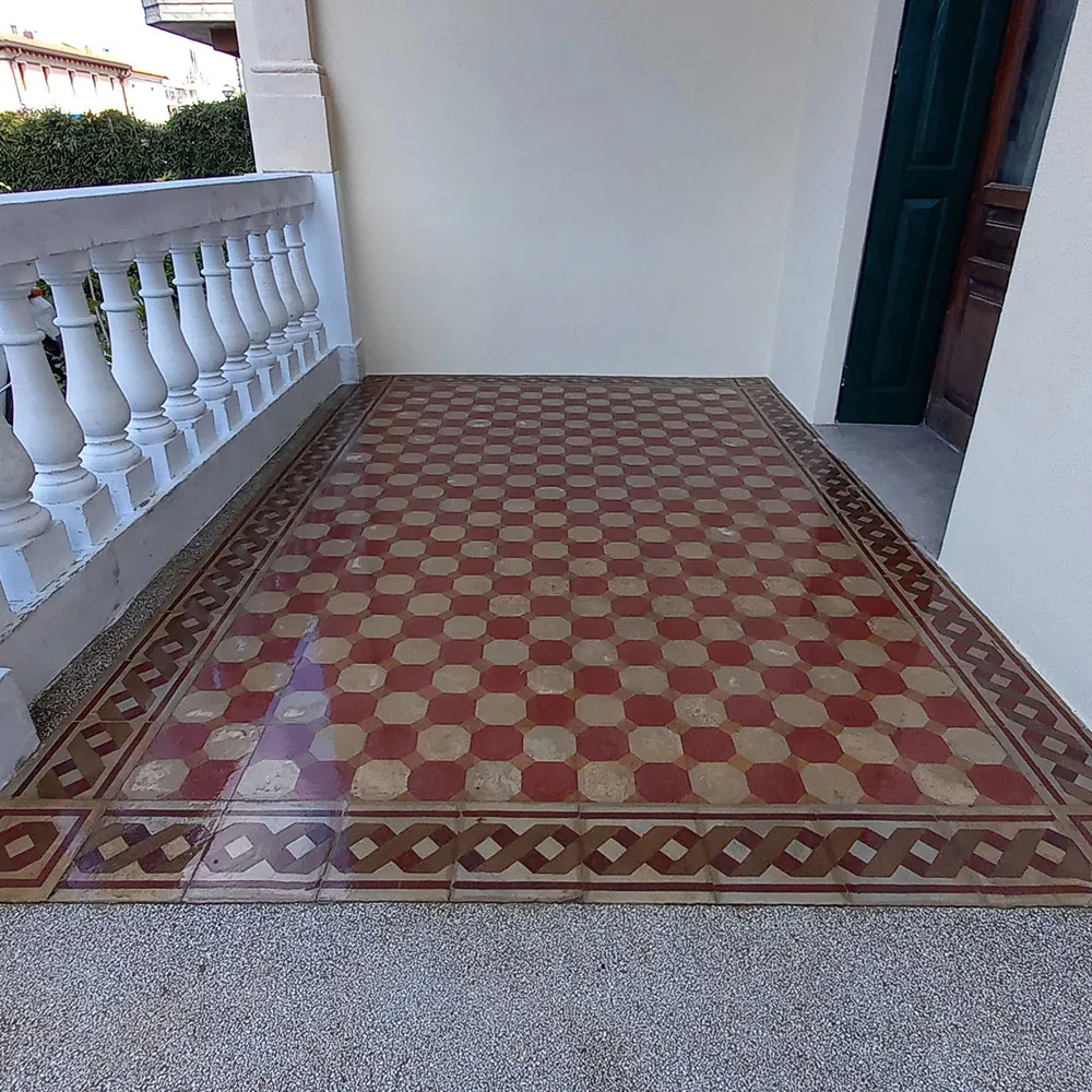 La stessa terrazza dopo il restauro: cementine rosse e avorio tornate brillanti, cornice a intreccio ben leggibile, balaustra ritinteggiata