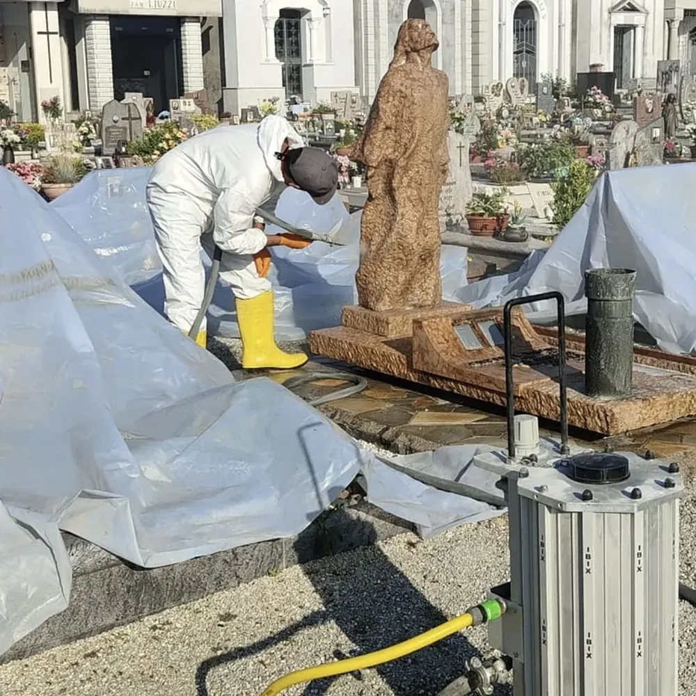 Operatore in tuta protettiva esegue la microsabbiatura della statua, con l'area circostante protetta da teli